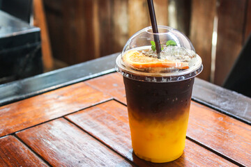iced yuzu orange juice infused with espresso coffee decorating with sliced orange piece in plastic cup on wooden table in coffee shop cafe 