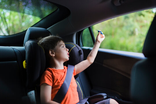 Cute boy playing with toy rocket on back seat of car