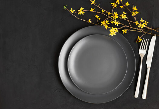 Black table setting. Yellow flowers and black plate on a dark gray background. Easter. Space for text. Top view, flat lay.