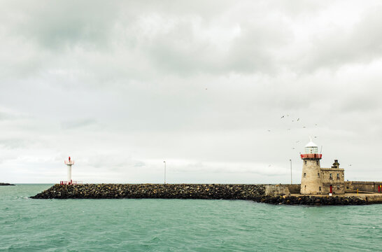 Lighthouse by sea against cloudy sky