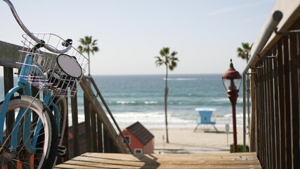 Blue bicycle, cruiser bike by ocean beach, pacific coast, Oceanside California USA. Summertime vacations sea shore. Vintage cycle by wooden stairs, stairway or staircase. Tropical palms and lifeguard