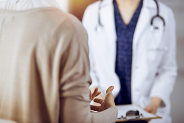 Doctor and patient discussing current health examination while sitting in sunny clinic. Medicine...