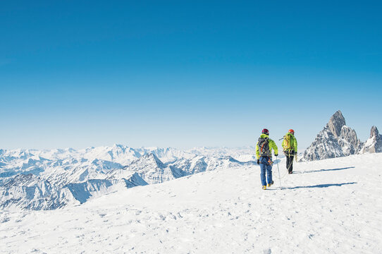 Rear view of hikers walking on snow covered mountain against clear blue sky