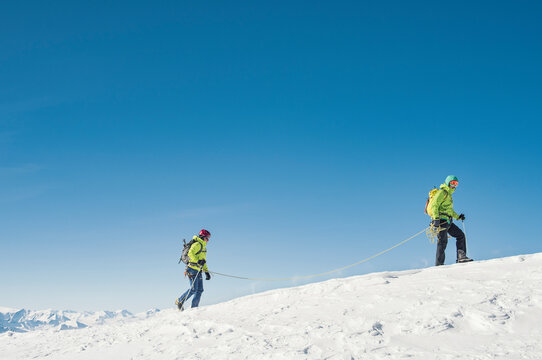 Side view of hikers walking on snow covered mountain against clear blue sky