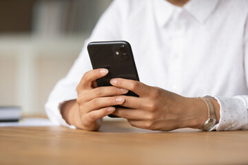 Crop close up of mixed race ethnicity woman sit at desk use modern smartphone text or message online. Ethnic woman hold cellphone browse wireless unlimited internet on gadget. Technology concept.
