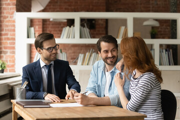 Happy Caucasian young couple clients consult with realtor or broker sign contract make agreement in...