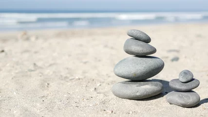 Fotobehang Zen Stenen Rock balancing on ocean beach, stones stacking by sea water waves. Pyramid of pebbles on sandy shore. Stable pile or heap in soft focus with bokeh, close up. Zen balance, minimalism, harmony and peace  © Dogora Sun