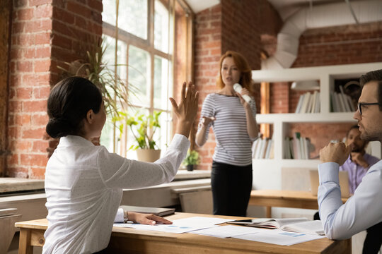 Back View Of Confident Ethnic Female Employee Raise Hand Ask Answer Question At Meeting With Coach Or Tutor. Woman Worker Volunteer Participate In Activity Or Training At Seminar In Office.