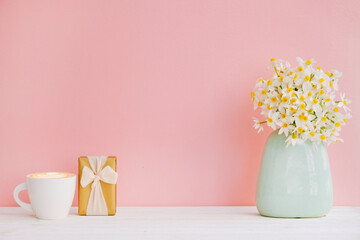 Lush bouquet of daffodils in vintage turquoise vase and cup of cappuccino isolated on pink background. Tender minimalistic spring flowers composition. Top view, copy space for text, flat lay, close up