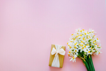 Lush bouquet of daffodils and a present in golden wrapping paper isolated on pink background. Tender minimalistic spring flowers composition. Top view, copy space for text, flat lay, close up.