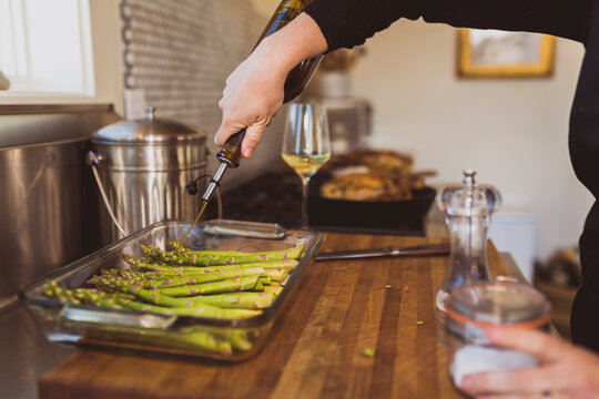 Cropped image of woman pouring cooking oil on asparagus in tray