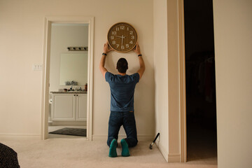 Rear view of man fixing clock on wall at home