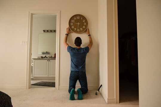 Rear view of man fixing clock on wall at home