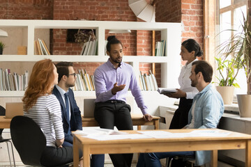 Confident young African American businessman lead meeting brainstorm with diverse employees in...