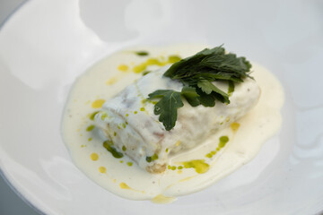 Scalding hot baked cabbage rolls with cream sauce close-up. Restaurant serving of cabbage rolls on a plate with greens.