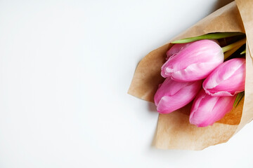 Obraz na płótnie Canvas A bouquet of pink french single late tulips in craft paper wrapping. Tender minimalistic spring flowers composition isolated on white background. Close up, copy space, top view, flat lay, studio shot.
