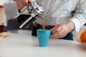Fototapeta na wymiar Elderly man using french press for coffee preparation and pouring it in mug. Senior person in the morning enjoying fresh brown cafe espresso cup caffeine from vintage mug, filter relax refreshment