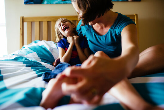 Mother tickling daughter's feet while sitting on bed
