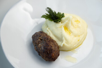Meat patty with mashed potatoes and herbs on a white plate. Restaurant dish close-up.