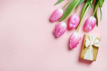 Multipurpose fresh flower composition, bouquet of pink tulips and a present wrapped in golden paper. International Women's day greeting concept. Copy space, close up, top view, flat lay, background.