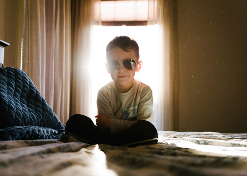 Portrait of boy with arms crossed wearing sunglasses while sitting on bed at home