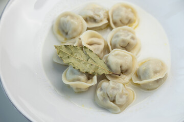 Meat dumplings on a white plate with bay leaf. Restaurant serving dishes, close-up.