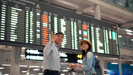 Couple traveler checking flight schedule board in airport terminal