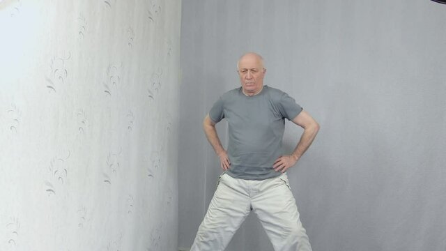 Old man in sportswear performs hip joint warm-up