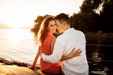 Gentle and touching hugs on a yacht against the background of water in the sea, a couple in love at sunset.