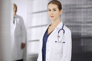 Cheerful female doctor standing in clinic. Portrait of friendly smiling woman physician. Perfect medical service in hospital. Medicine concept