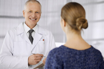 Elderly confident doctor consults woman patient in clinic. Perfect medical service in hospital. Medicine and healthcare concept