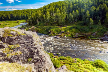 Fast river with rocky banks, overgrown with trees in summer