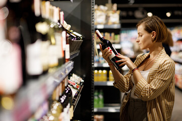 young girl are shopping at a supermarket. girl are choosing drinks. Alcohol drinks - obrazy, fototapety, plakaty