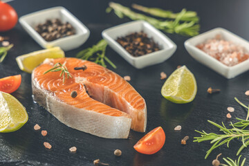 Fresh raw salmon steak on blackstone cutting board with salt, peppers, lime, and rosemary, close up