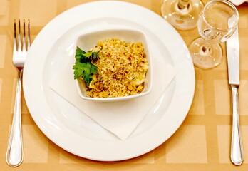 Salad with a sprig of parsley on a white ceramic plate, metal spoon and fork, glass glass close-up on the background of the tablecloth