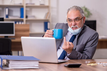 Obraz premium Coronavirus infected old businessman employee sitting in the off