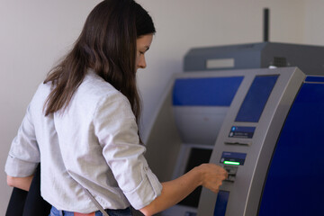 Young woman uses ATM to withdraw cash or pay for services,