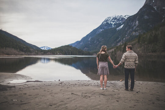 Rear view of young couple holding hands while standing on lakeshore at Silver Lake Provincial Park