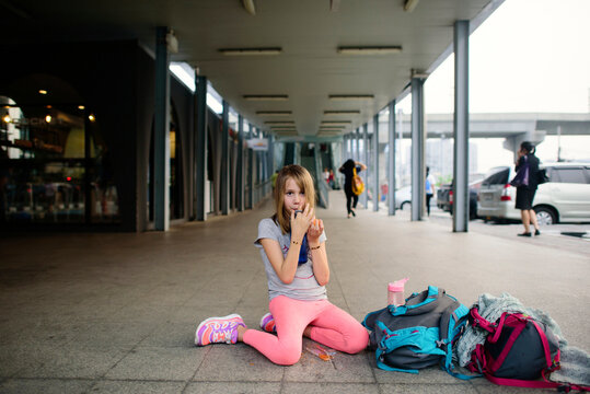 Girl drinking from water bottle while kneeling at sidewalk