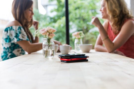 Female friends having coffee together at cafe with smart phones on table