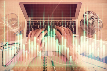 Double exposure of man's hands typing over laptop keyboard and forex chart hologram drawing. Top...