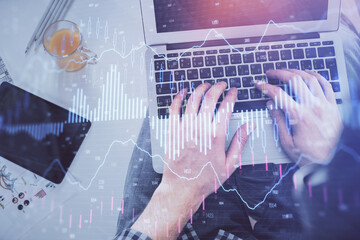 Double exposure of man's hands typing over laptop keyboard and forex chart hologram drawing. Top view. Financial markets concept.