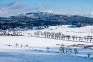 Fototapeta na wymiar Winter hilly landscape scenery with snow, trees, houses in the Czech Republic
