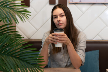 young woman sits at a table in a cafe and communicates on the Internet in mobile apps,