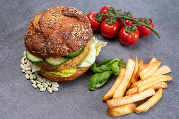 Tasty vegetarian vegan lunch with hamburger made from vegetables based burger, organic bun with seeds and fresh vegetables and french fried potatoes