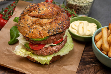 Tasty vegetarian vegan lunch with double decker hamburger made from plant based soya beans burger, organic bun with seeds and fresh vegetables and french fried potatoes