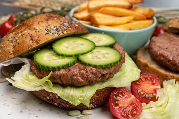 Tasty vegetarian vegan lunch with hamburger made from plant based soya beans burger, organic bun with seeds and fresh vegetables and french fried potatoes