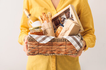 Woman holding gift basket with products on light background, closeup