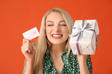 Beautiful young woman with gift card and present on color background