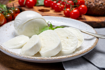 Cheese collection, eating. of white soft Italian cheese mozzarella, served with red cherry tomatoes, fresh basil leaves